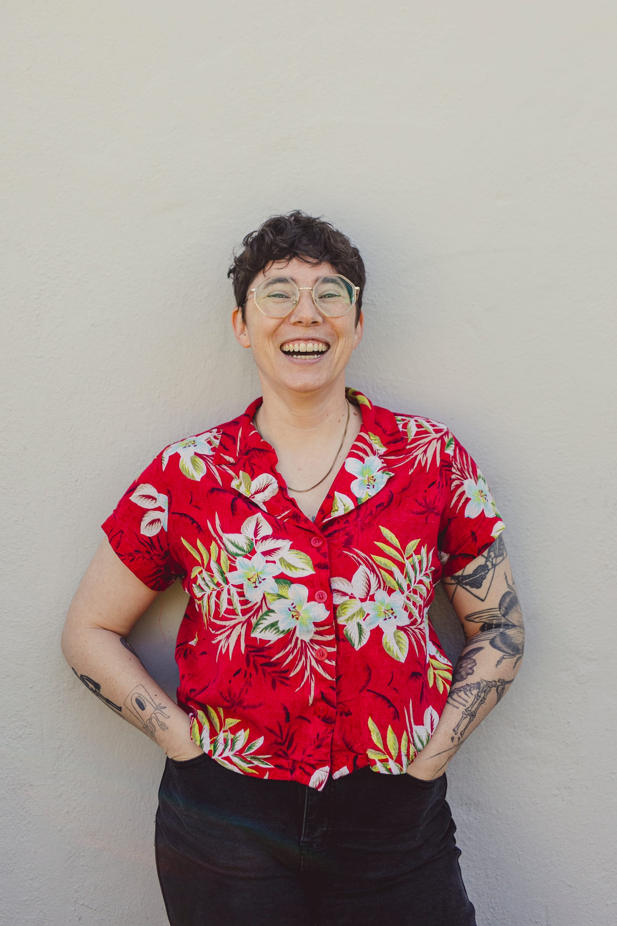 A photo of a person (me) wearing a red Hawaiian shirt standing in front of a grey wall. I am laughing.