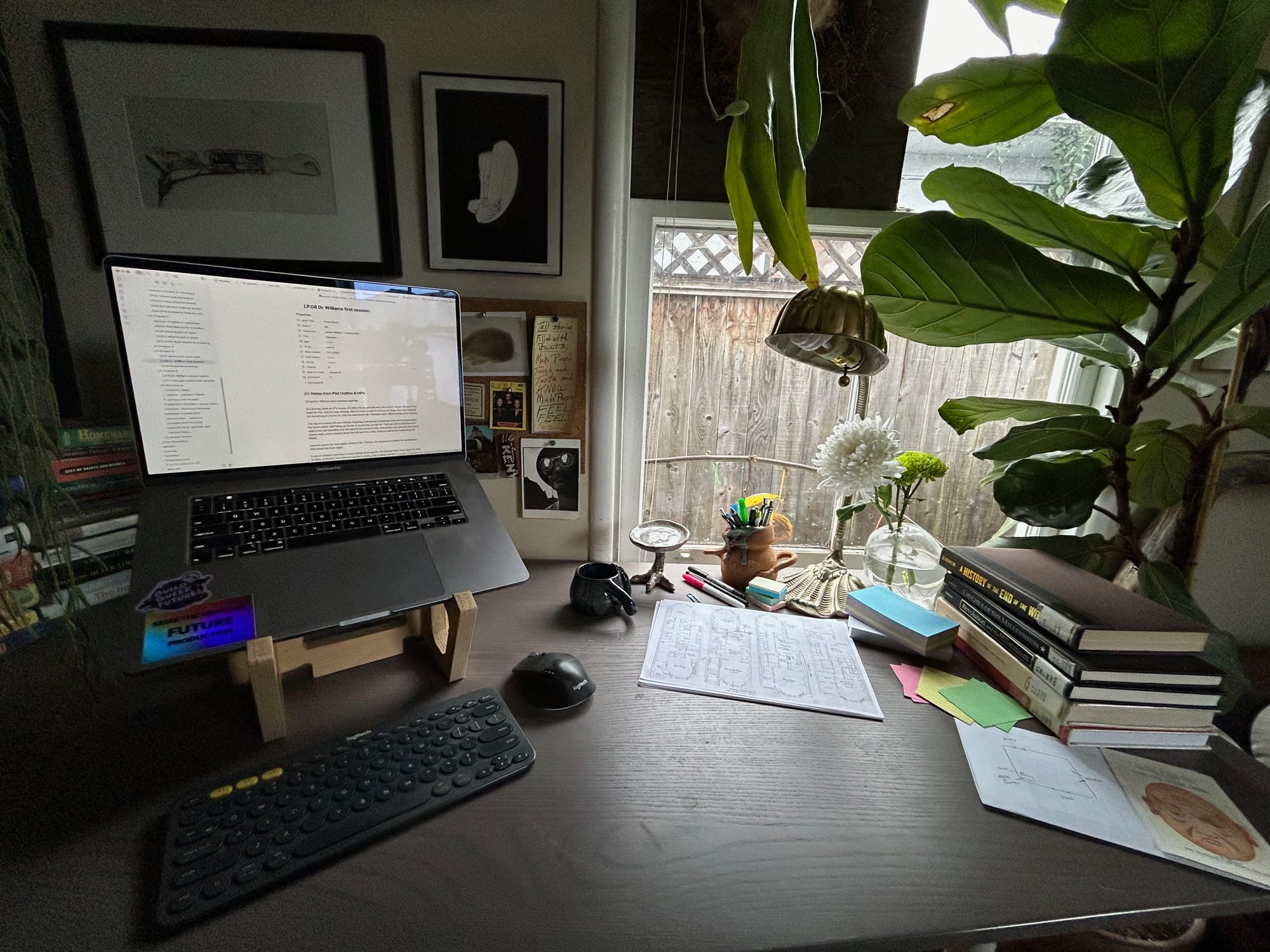 a desk with a computer and a stack of books and plants on it