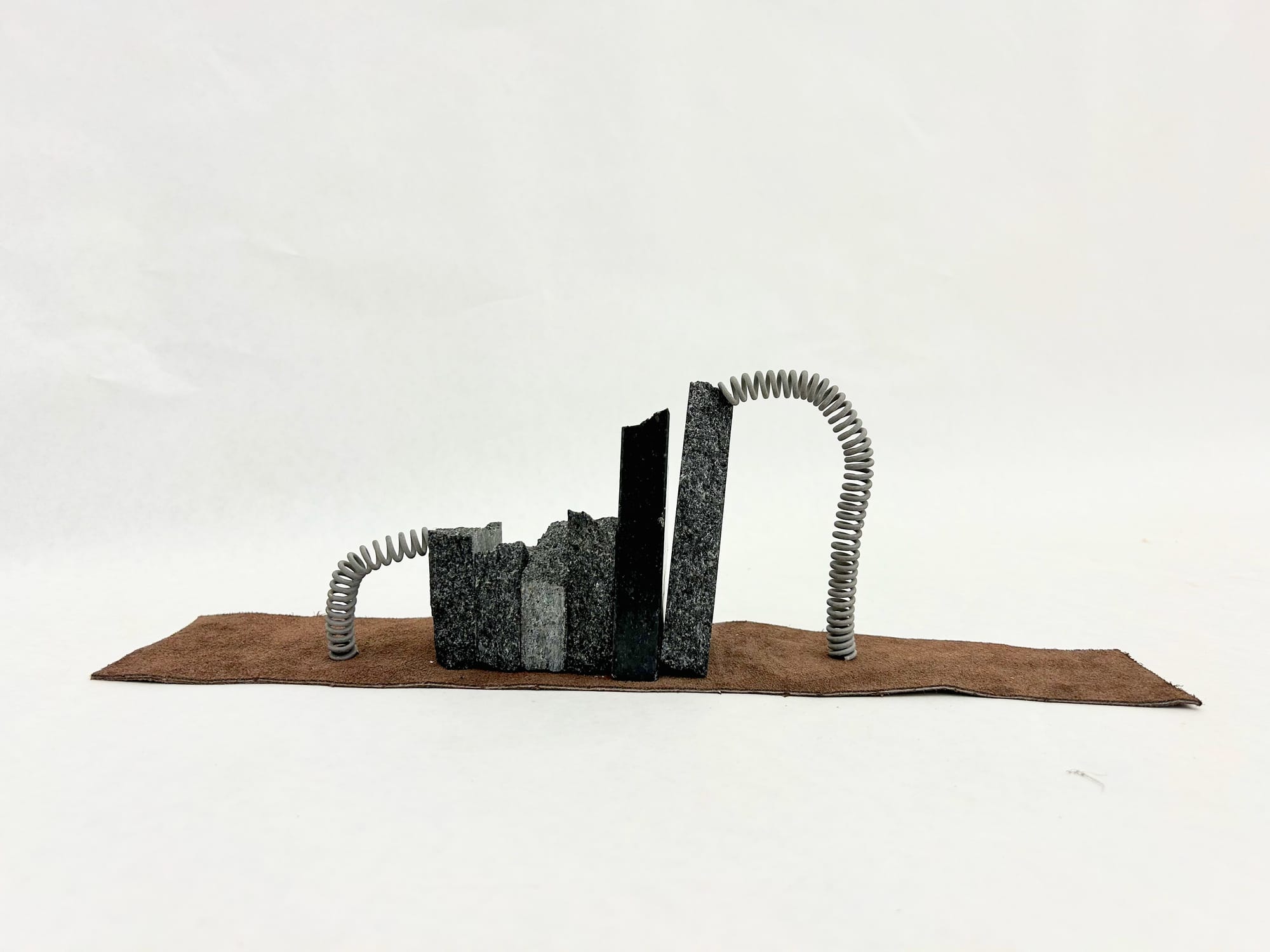 a small sculpture made of a row of black marble pieces being held together by a silver metal coil, sitting on a strip of brown leather