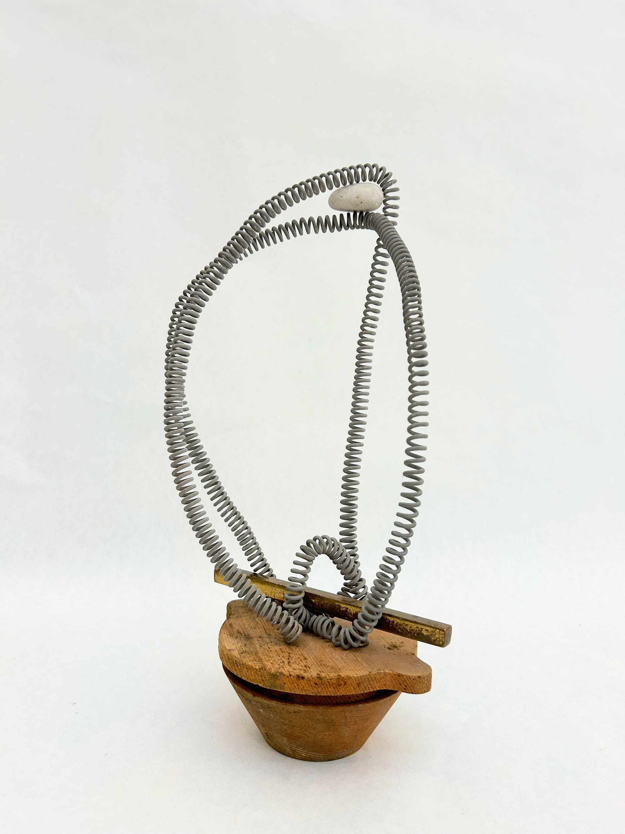 a small sculpture made of a wooden base, a brass strip, and some loops of silver coils - at the top there is a rock balanced between two of the coils