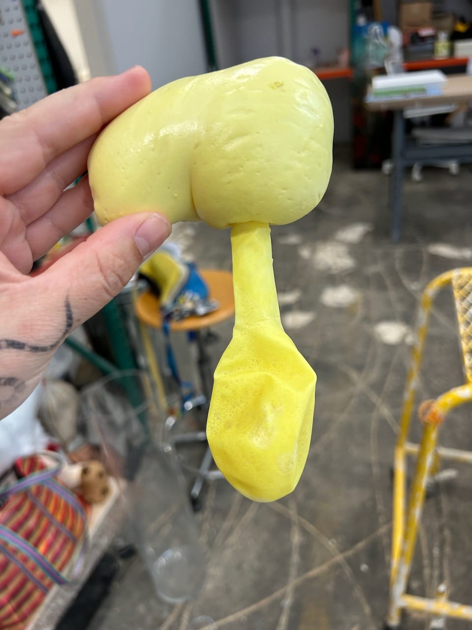 a hand holding a piece of yellow spray foam shaped like a balloon
