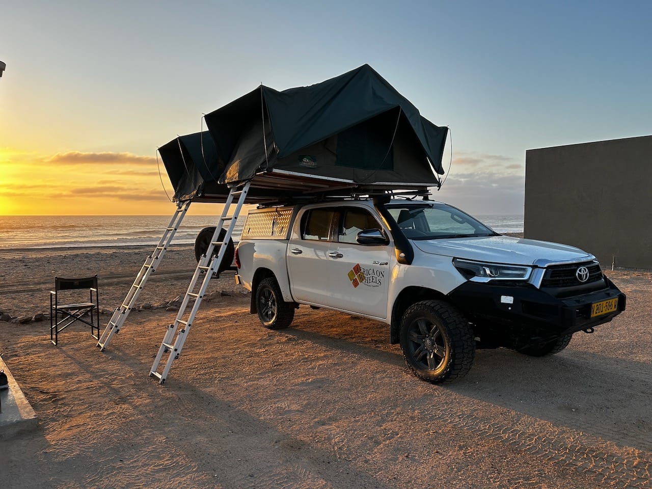 A white pickup truck with two tents on top with ladders that extend down to the ground.