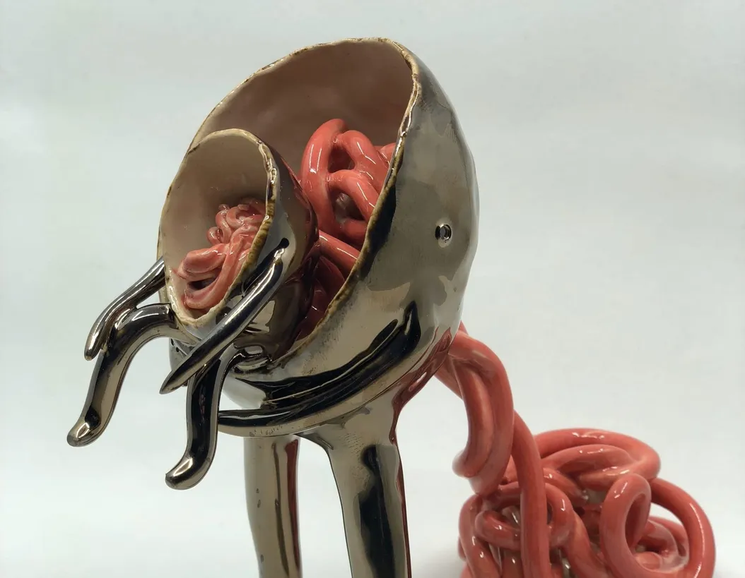 a ceramic sculpture of an abstract body, holding a smaller body, with noodles coming out of them
