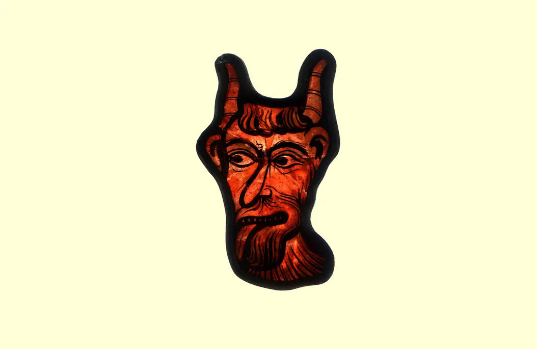 A piece of red stained glass painted to look like the devil sticking his tongue out.